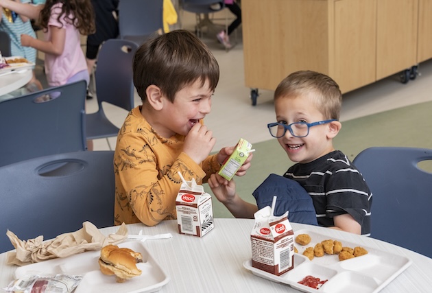 Two boys laugh while eating lunch.