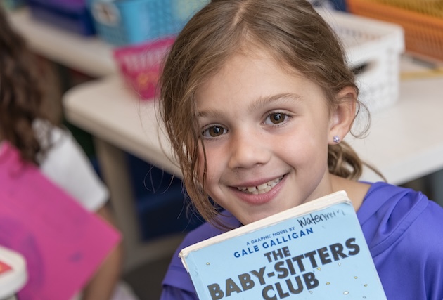 A young girl stops to pose while reading.