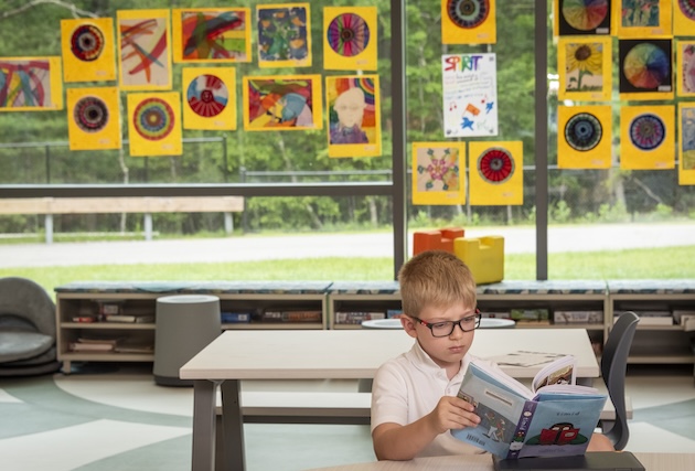 A young boy is reading a book in the empty cafeteria.