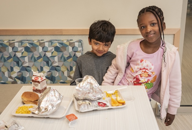 Two students standing at a table with food on it.