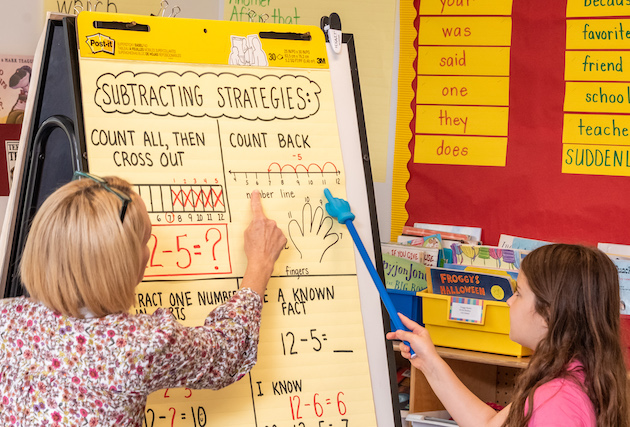 A teacher and student working at a piece of chart paper