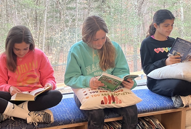 Three Girls sitting in the window area reading a book